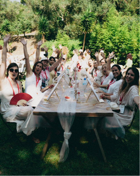 Grupo de mulheres celebrando em uma mesa ao ar livre, em um encontro Uma Nova Mulher